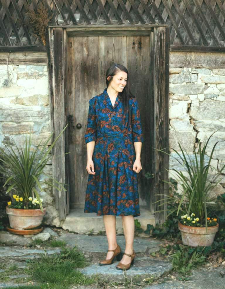 Brunette white women smiling standing slightly turned to the left in front of a white studio backdrop, wearing 247 Lindy Shirtdress, and heels.