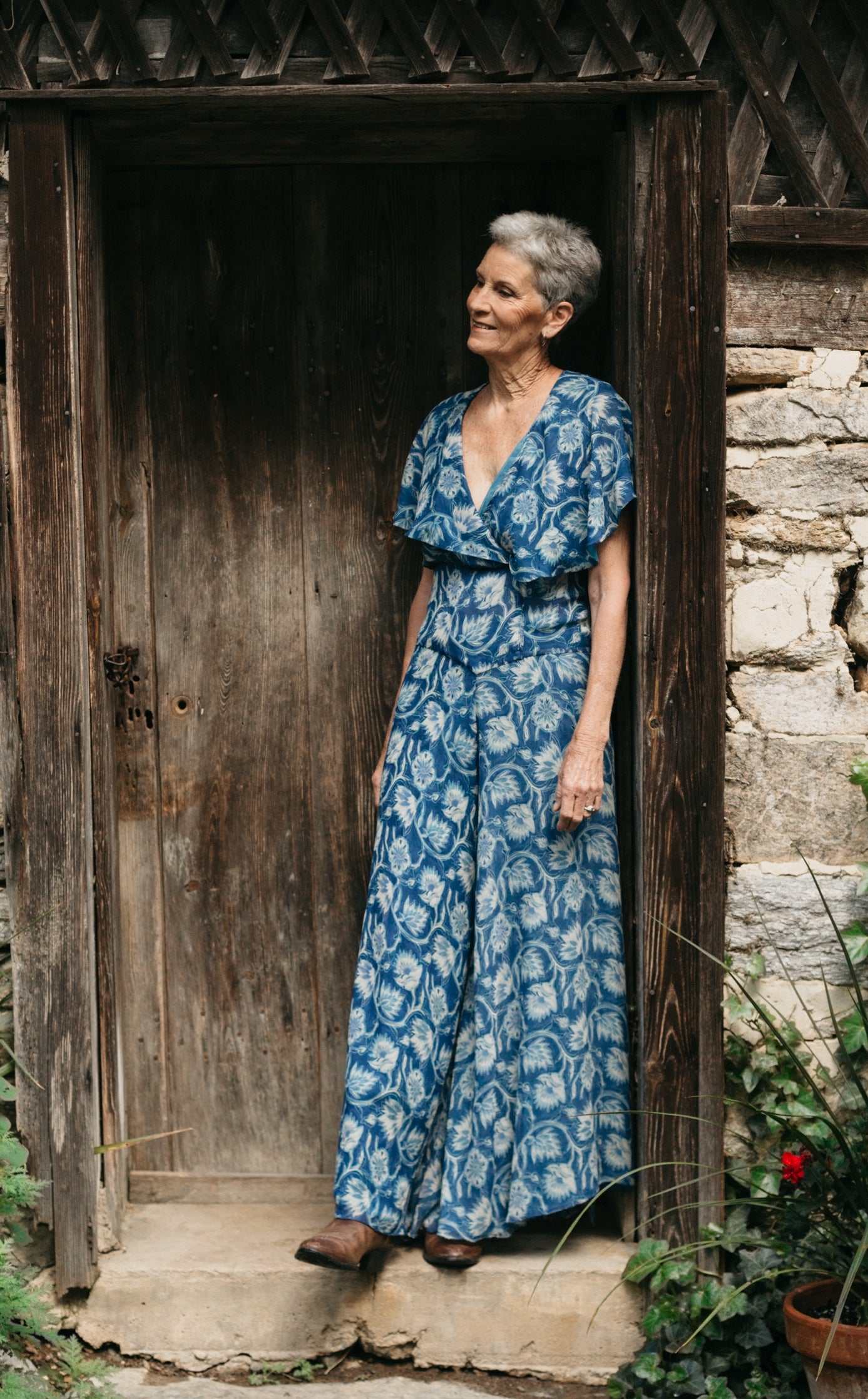 Woman in blue silk beach pyjamas leaning in doorway of stone building.