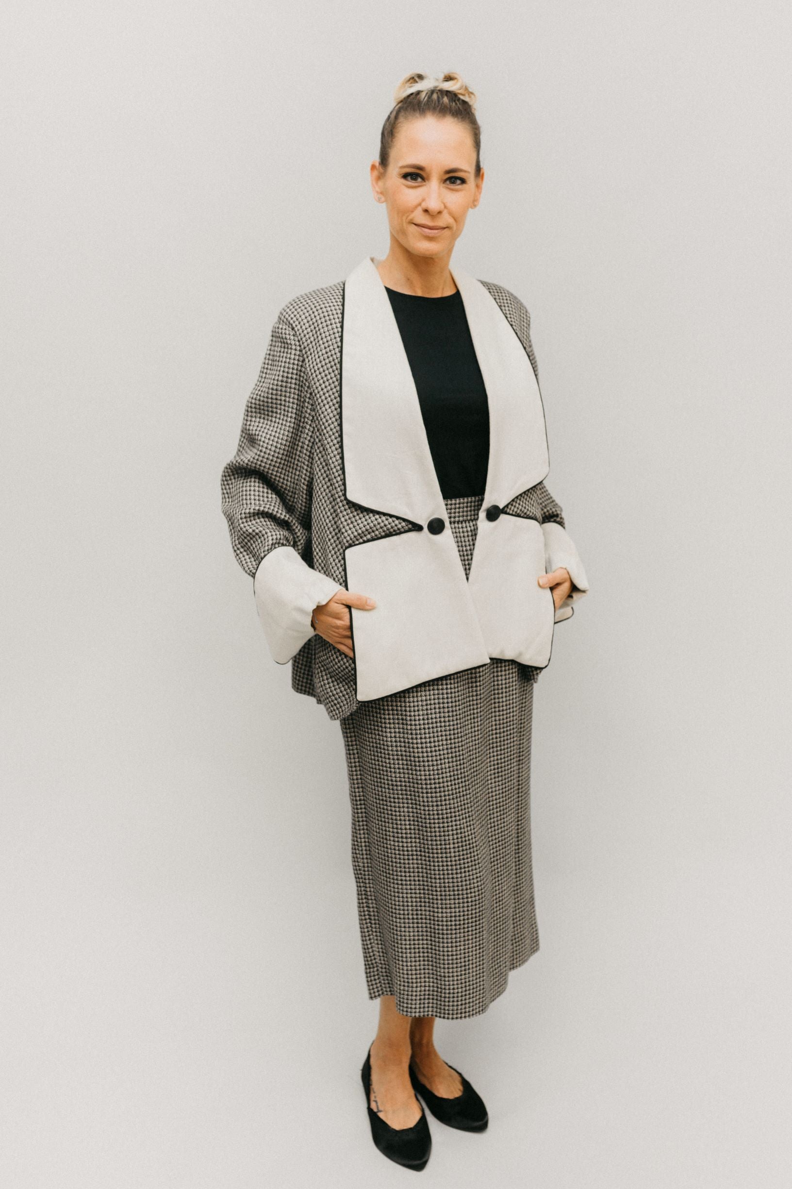 White woman standing in front of a white studio backdrop wearing #255 Swing Suit with hands in pockets.