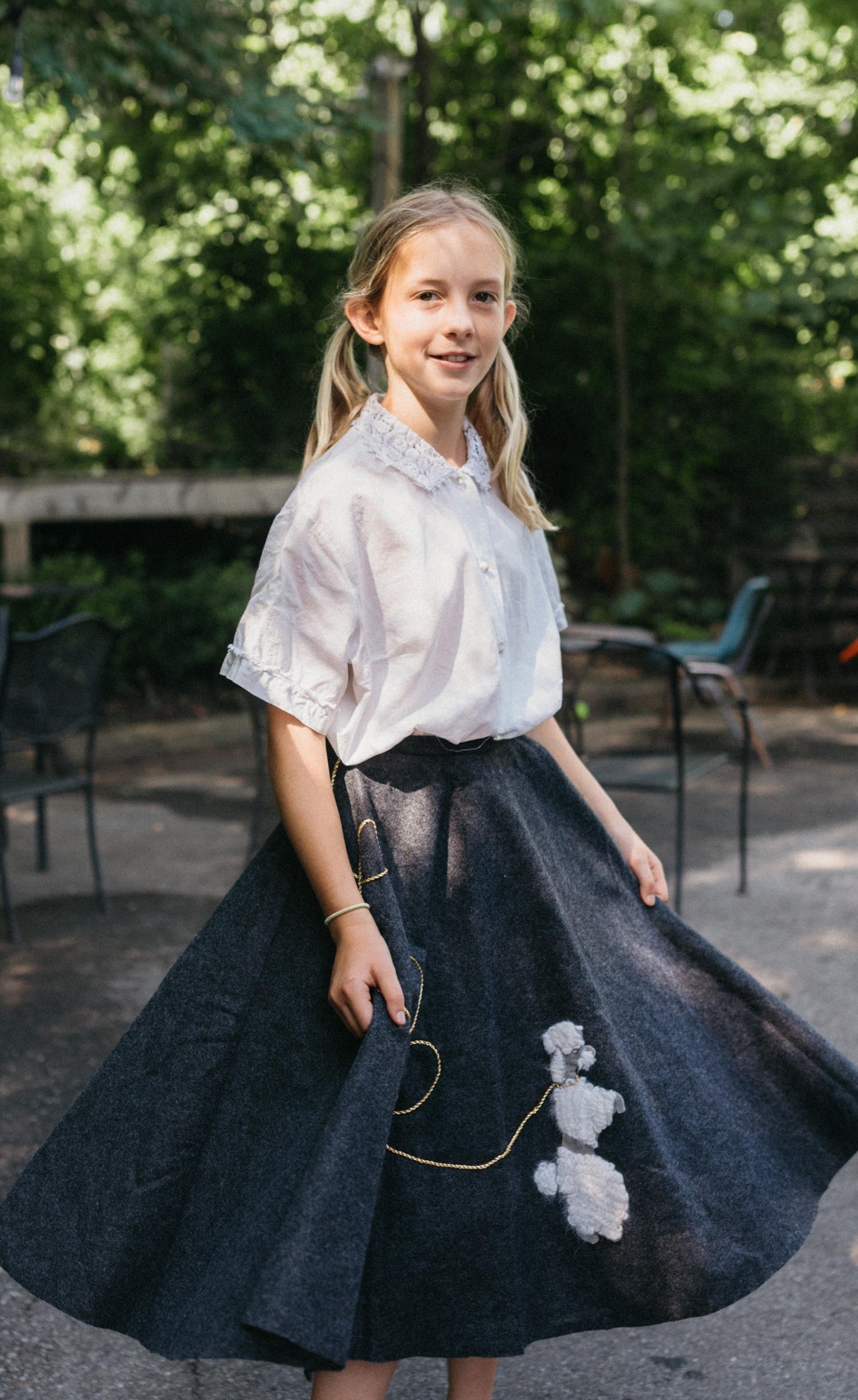 Young blonde girl wearing blouse and skirt of #256 At The Hop surrounded by greenery.