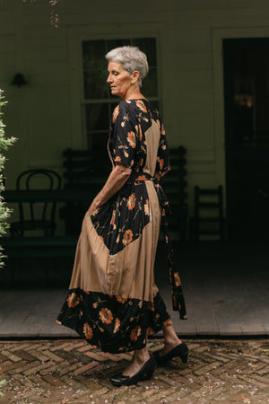 Older White woman with grey hair, wearing #261 Paris Promenade Dress, turned to the side standing in front of a porch.