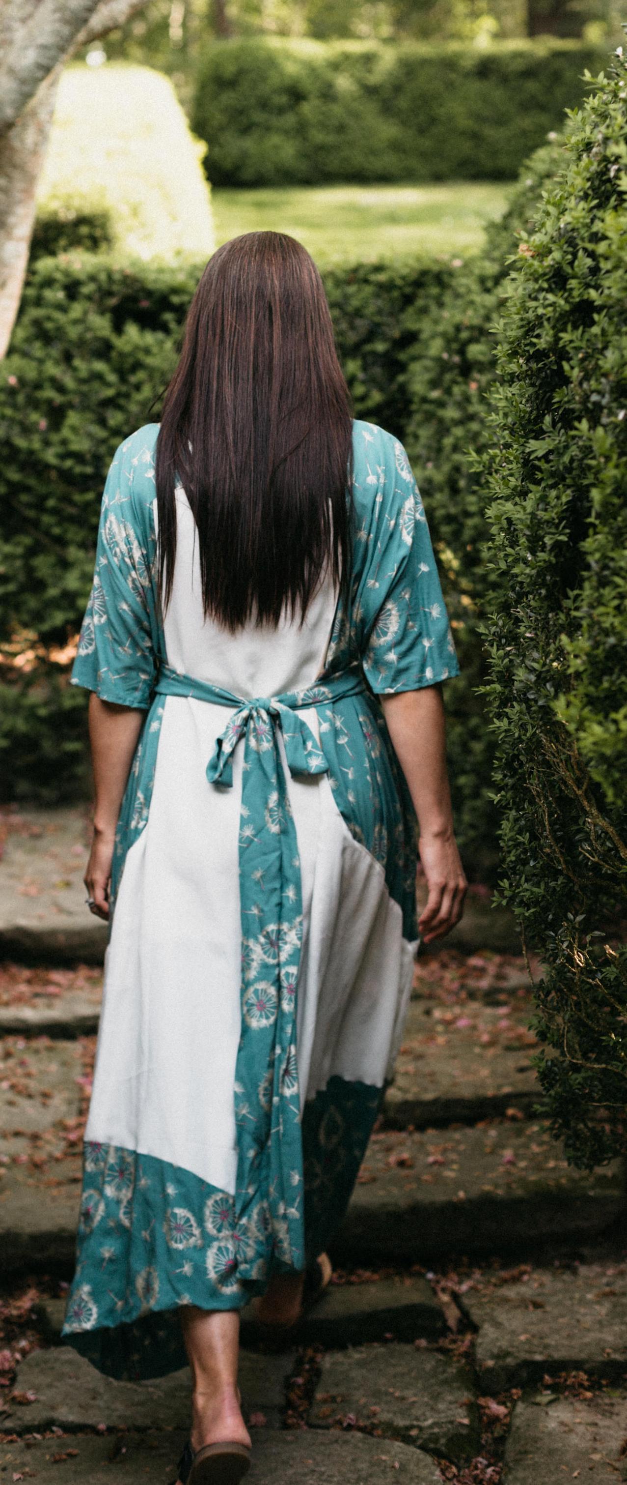 brunette woman walking up steps surrounded by greenery showing the back view of the Paris Promenade Dress.