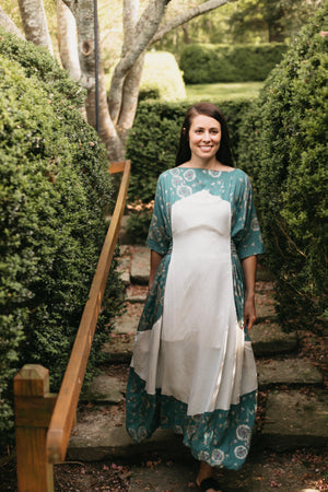 Young Brunette woman smiling walking down steps surrounded by greenery wearing the #261 Paris Promenade Dress.