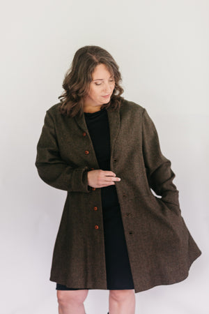 Brunette White woman standing in front of a studio white backdrop wearing a black dress under the #263 Countryside Frock Coat with her left hand in the pocket.