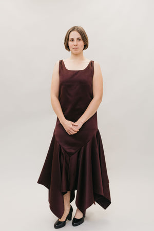 Young Burnett White woman with neck length hair, standing in front of a studio white backdrop wearing the #264 Monte Carlo Dress in maroon., with black pumps. 
