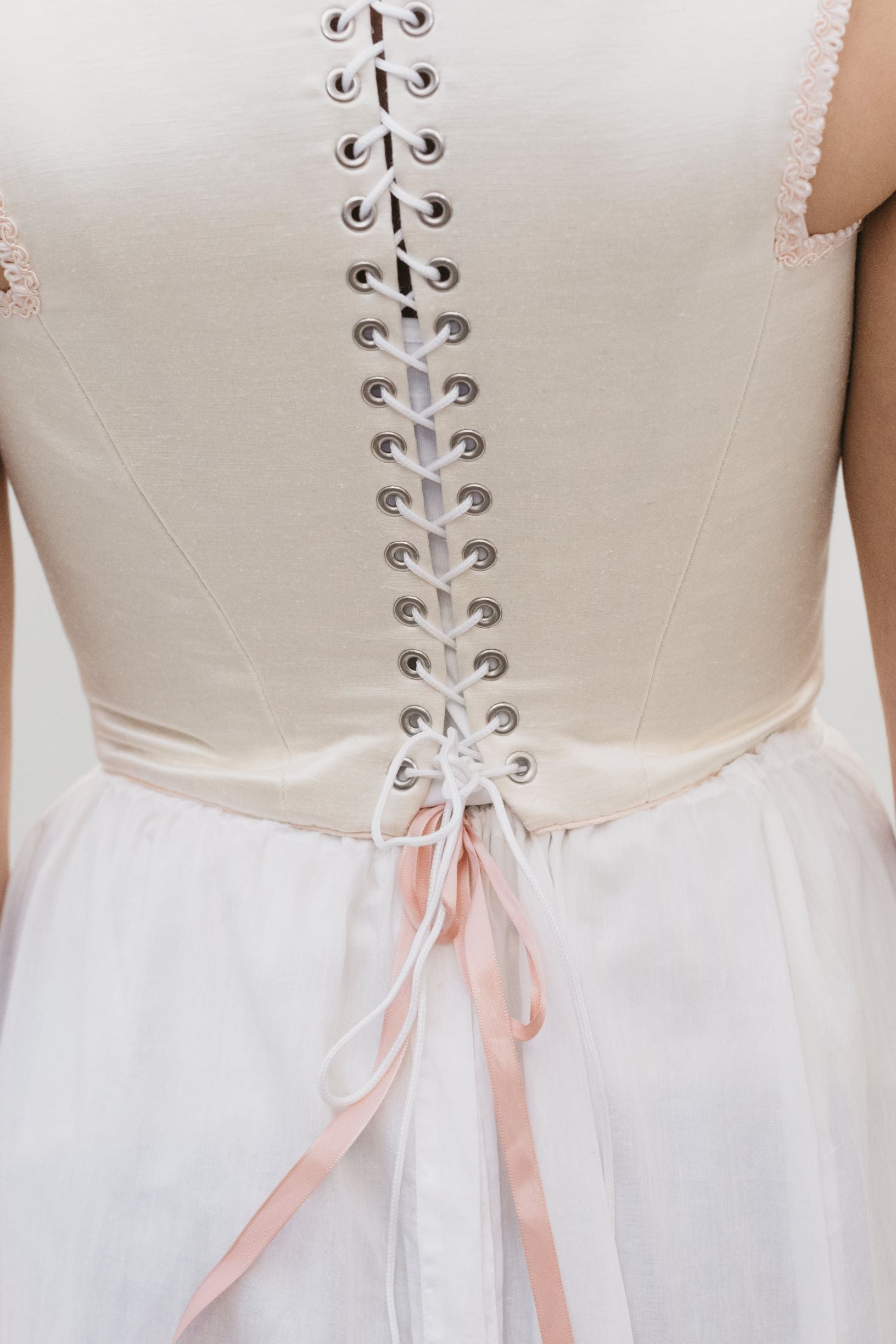 Back view of square neck Lady's Corset laced in the back in white. Pink ribbons show on a slip chemise