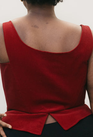 Close up back view of Black woman with shorter curly hair, wearing red #267 M' Lady's Corset with a scoop neck and black pants, standing in front of a studio white backdrop with her left hand on her hip showing how the pattern can be made for a DIY corset top. Romantic and sexy.