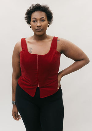 Black woman wearing red #267 M' Lady's Corset with a scoop neck and black pants, standing in front of a studio white backdrop with her left hand on her hip showing how the pattern can be made for a DIY corset top. Romantic and sexy.