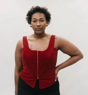 African American woman wearing the Lady's Corset scoop neck in red, left hand on her hip standing in front of a studio white backdrop.