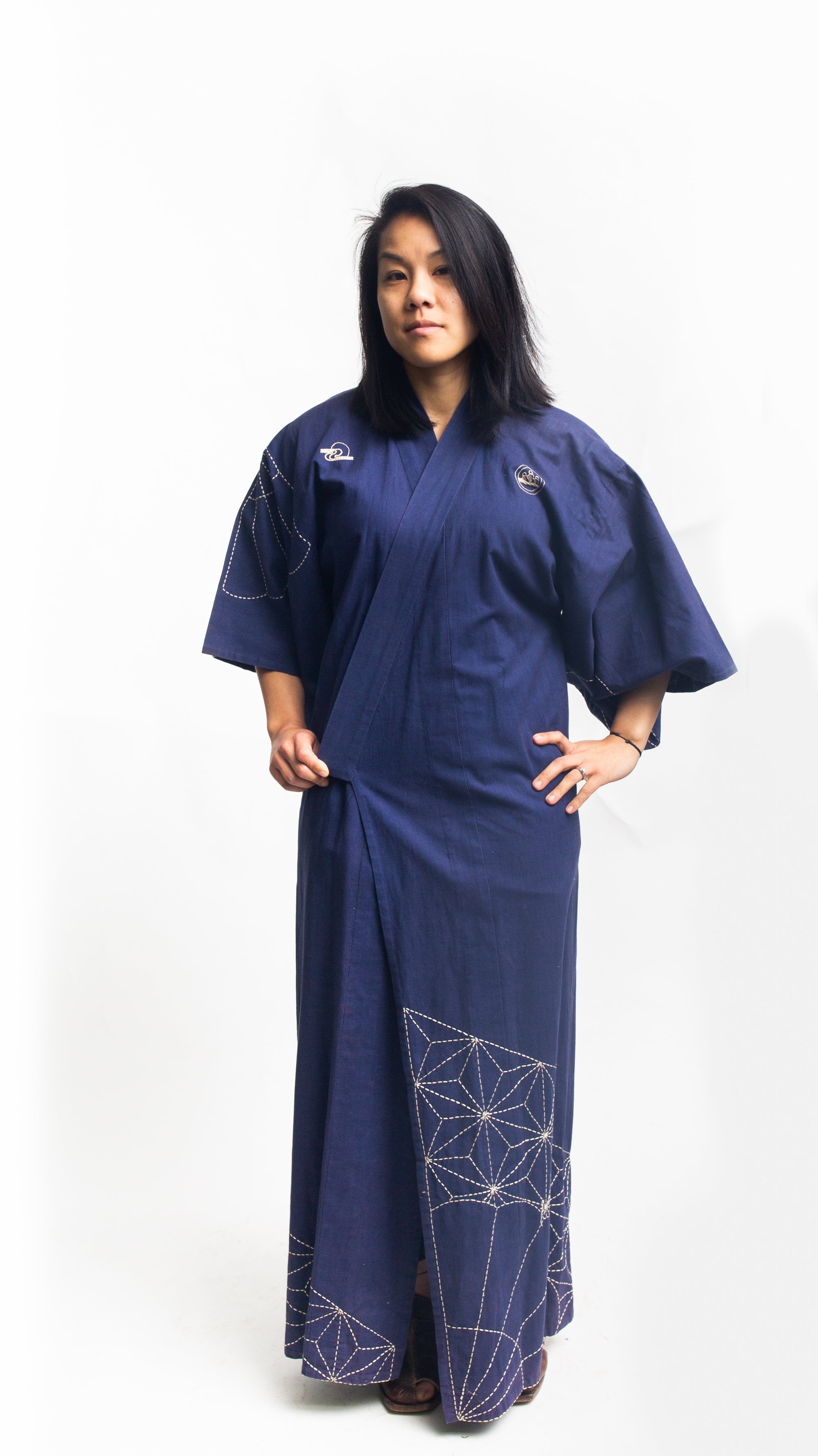 Asian American woman wearing a navy embroidered kimono standing in front of a white background.