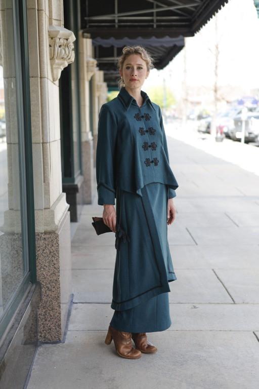 Young blonde white woman standing outside of a shop with her knee bent wearing the Metropolitan Suit. 