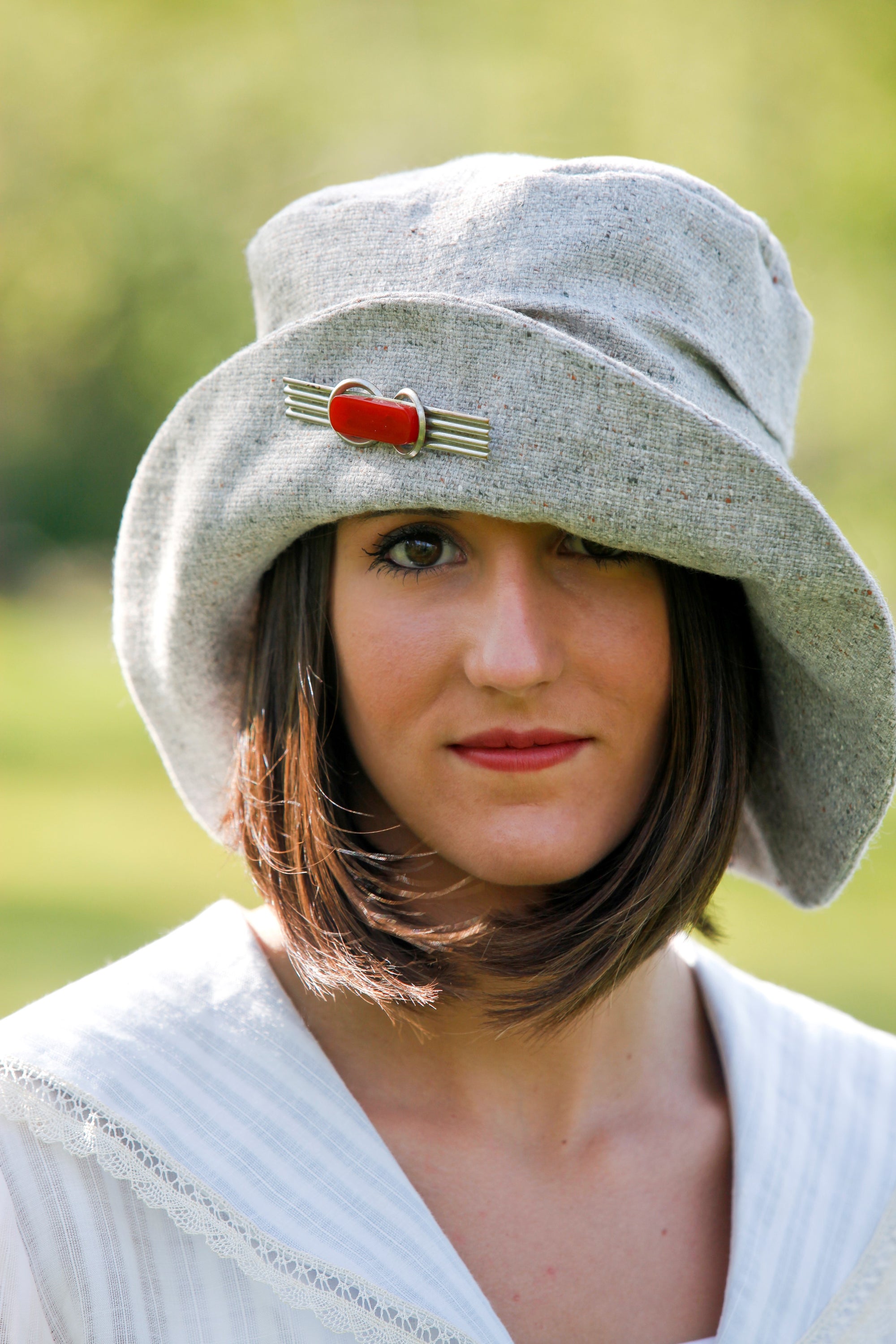 Young brunette white women wearing red lipstick. Wearing the #269 Metropolitan Hat in gray with a red brooch on the brim of the hat.