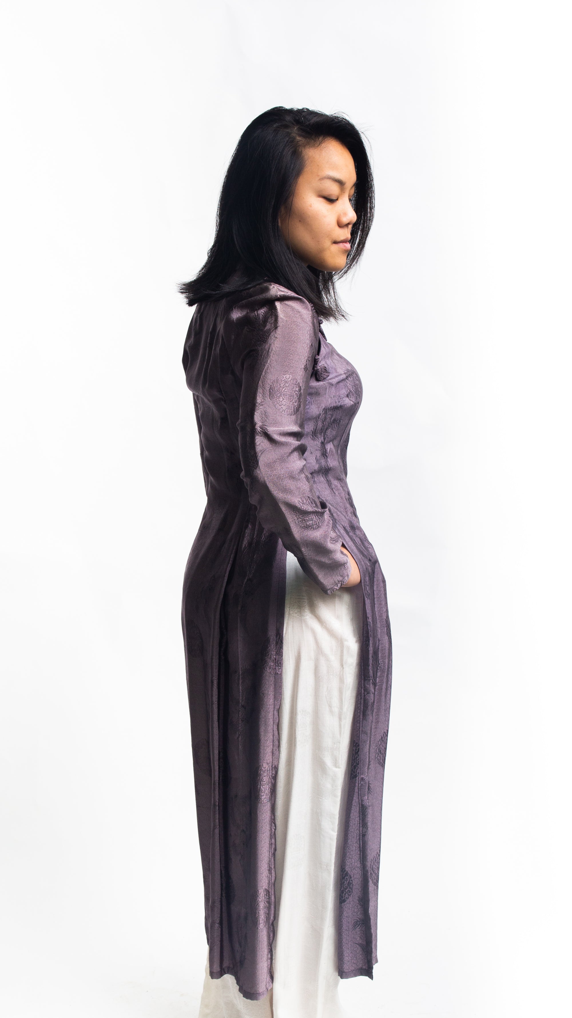 Side view of Vietnamese American woman wearing a purple silk Ao Dai tunic with white pants.