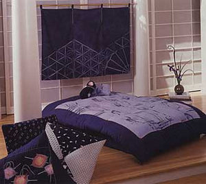 Picture of a Japanese Interior , with a futon and blue futon covers with a top quilt,  with blue floor cushions. Decorative blue curtain on the back wall 