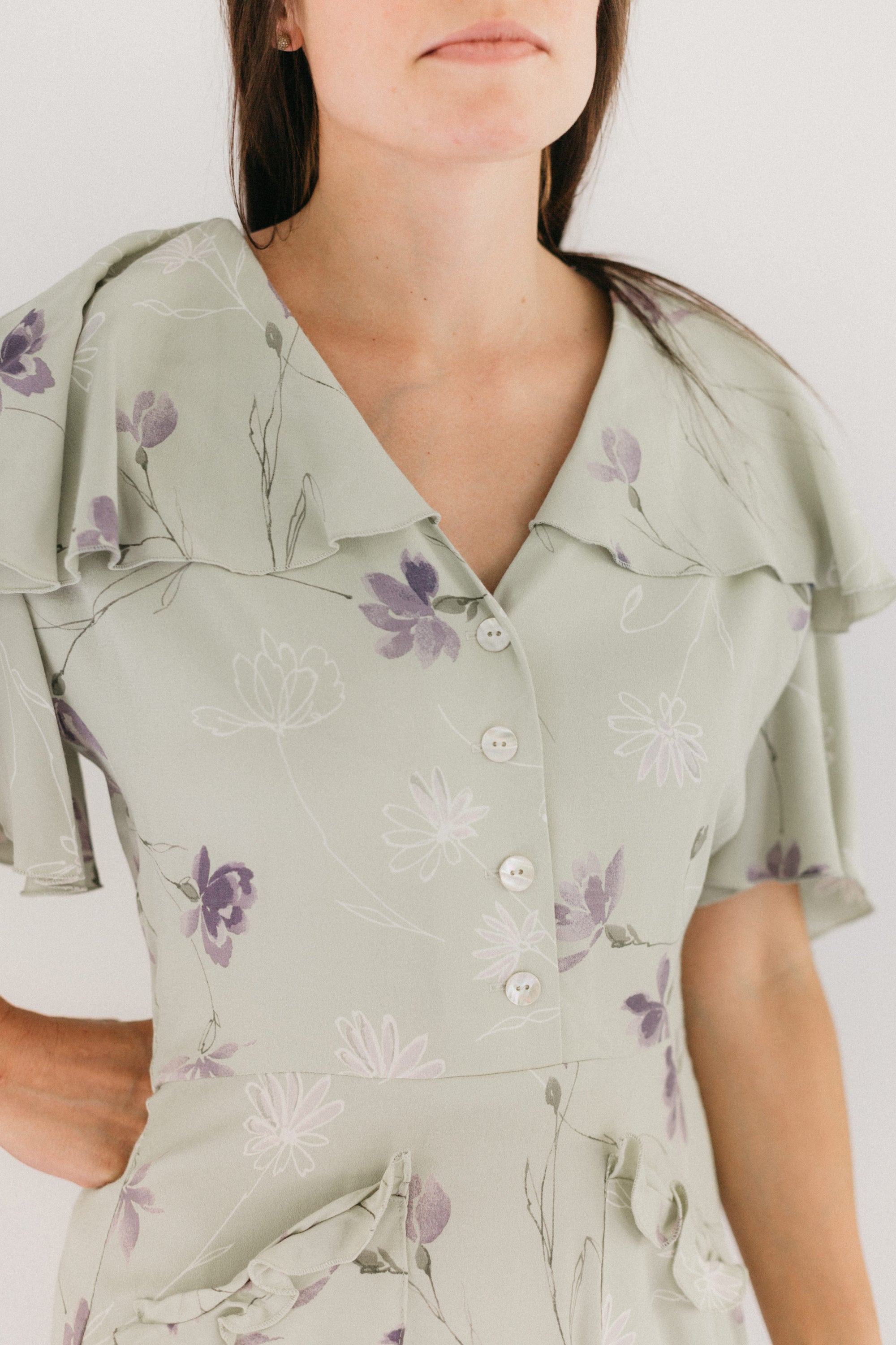 Close up photo of woman in light mint green and lavendar dress.  View B.  Shows the  button front closure and the flounced neckline. View B is more casual, with buttoned front, flounce collar and sleeves, and eyelash pockets.