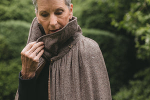 Older white woman with gray hair surrounded by greeneryclose up of her holding the collar upturned. 