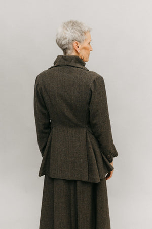 Older white woman standing in font of a white studio backdrop, wearing the traveling suit back facing the audience showing the flared below the hip peplum and the high stand collar  