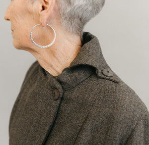 Older white woman wearing sliver hooped earnings ,close up of her left shoulder and neck wearing the Traveling Jacket buttoned on the left side on the neck, with a contrast over collar 