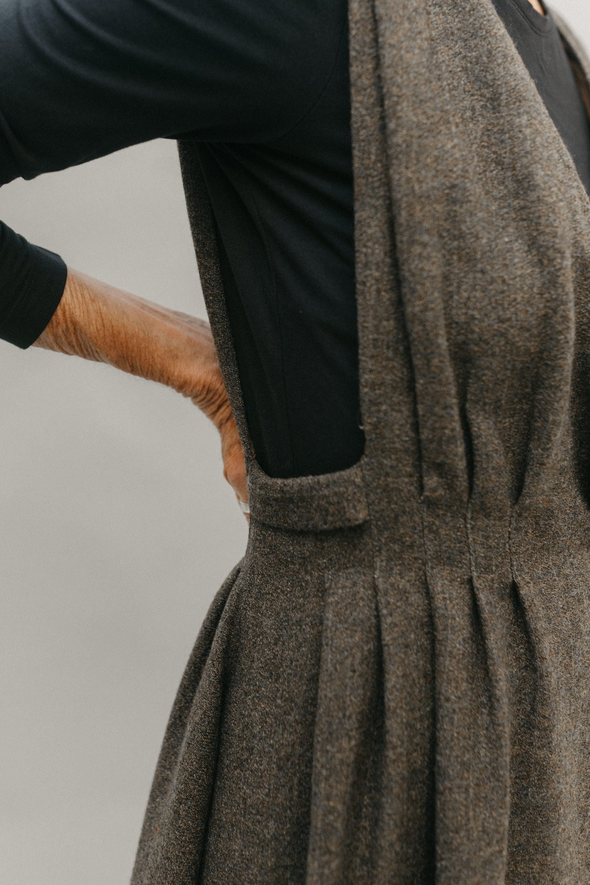 Woman standing with right arm on her back , wearing a black long sleeved underneath the jumper, close up of the armscyces open to just above the waist with pleats.