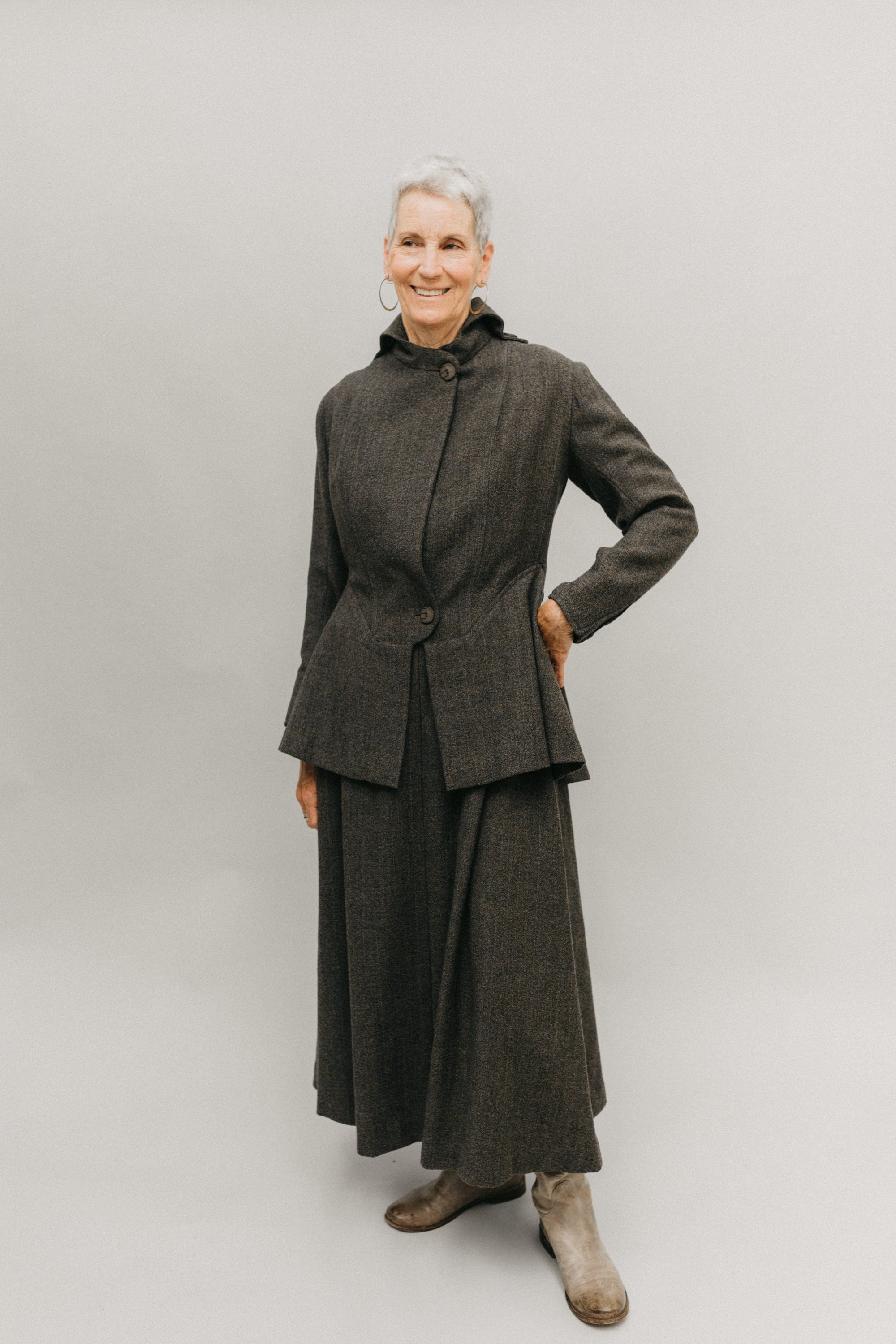 Older white woman smiling, standing her left hand on her hip, in front of a studio white backdrop wearing the 508 traveling suit buttoned