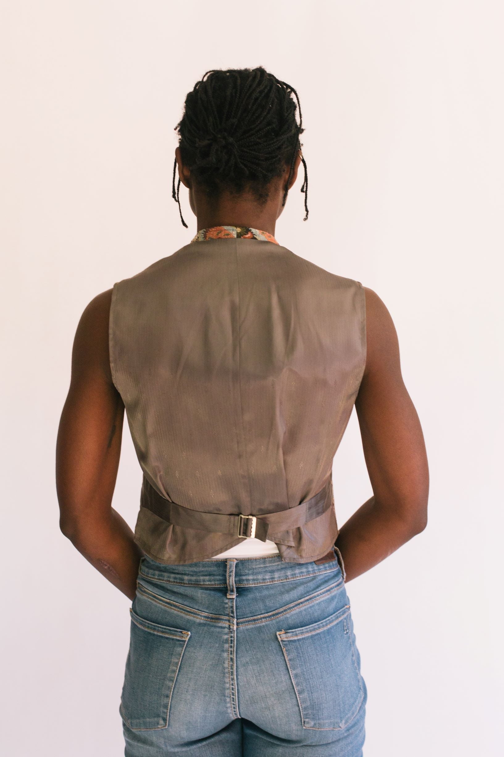 Back view of African woman standing in front of a white studio backdrop wearing View A 222 Vintage Vests, with adjustable back waist belt.