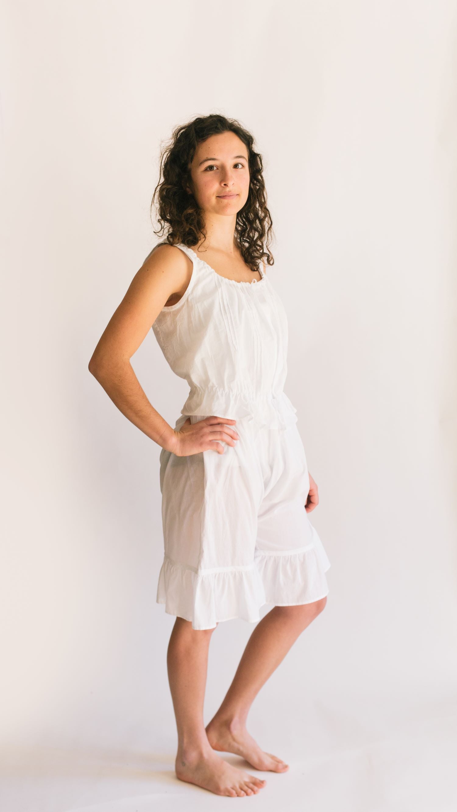 Photo of young woman standing in front of a white studio backdrop wearing camisole and drawers.