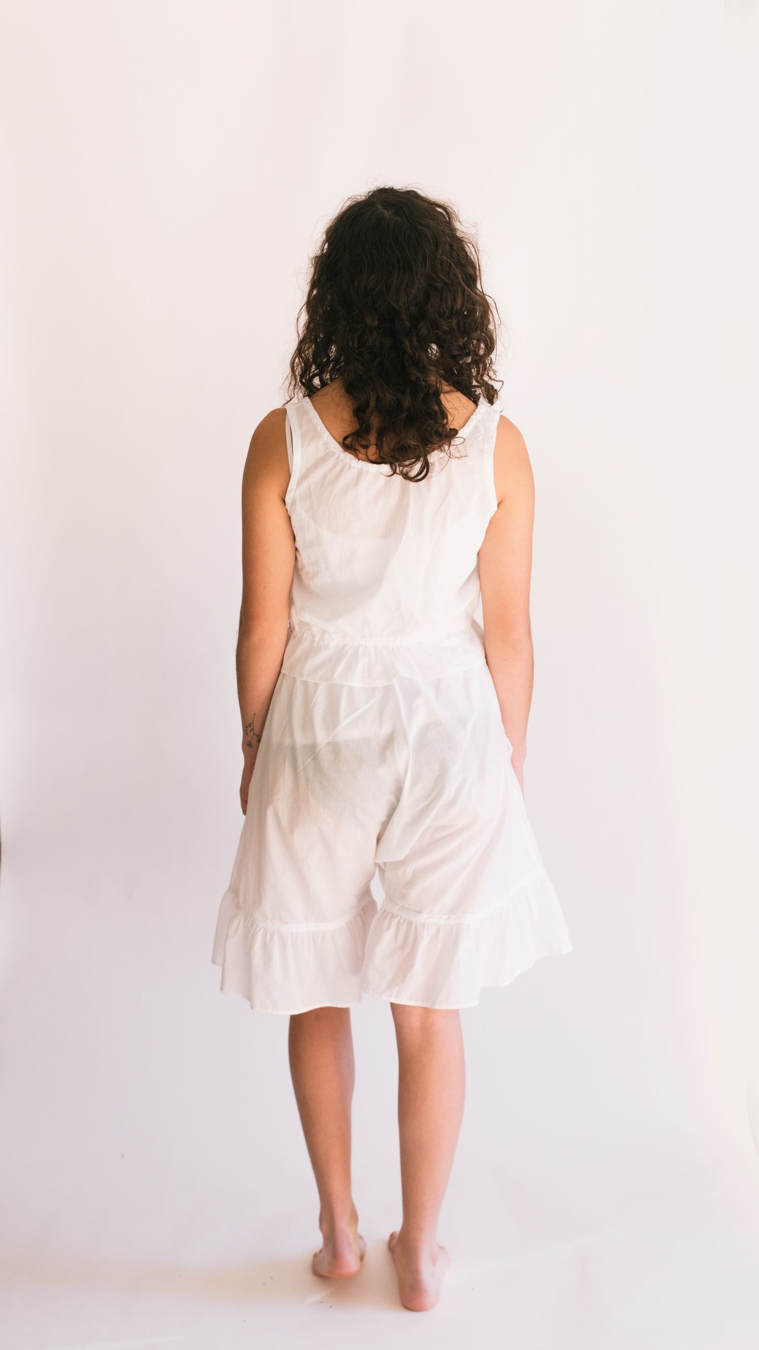 Photo of back view of young woman wearing camisole and drawers.