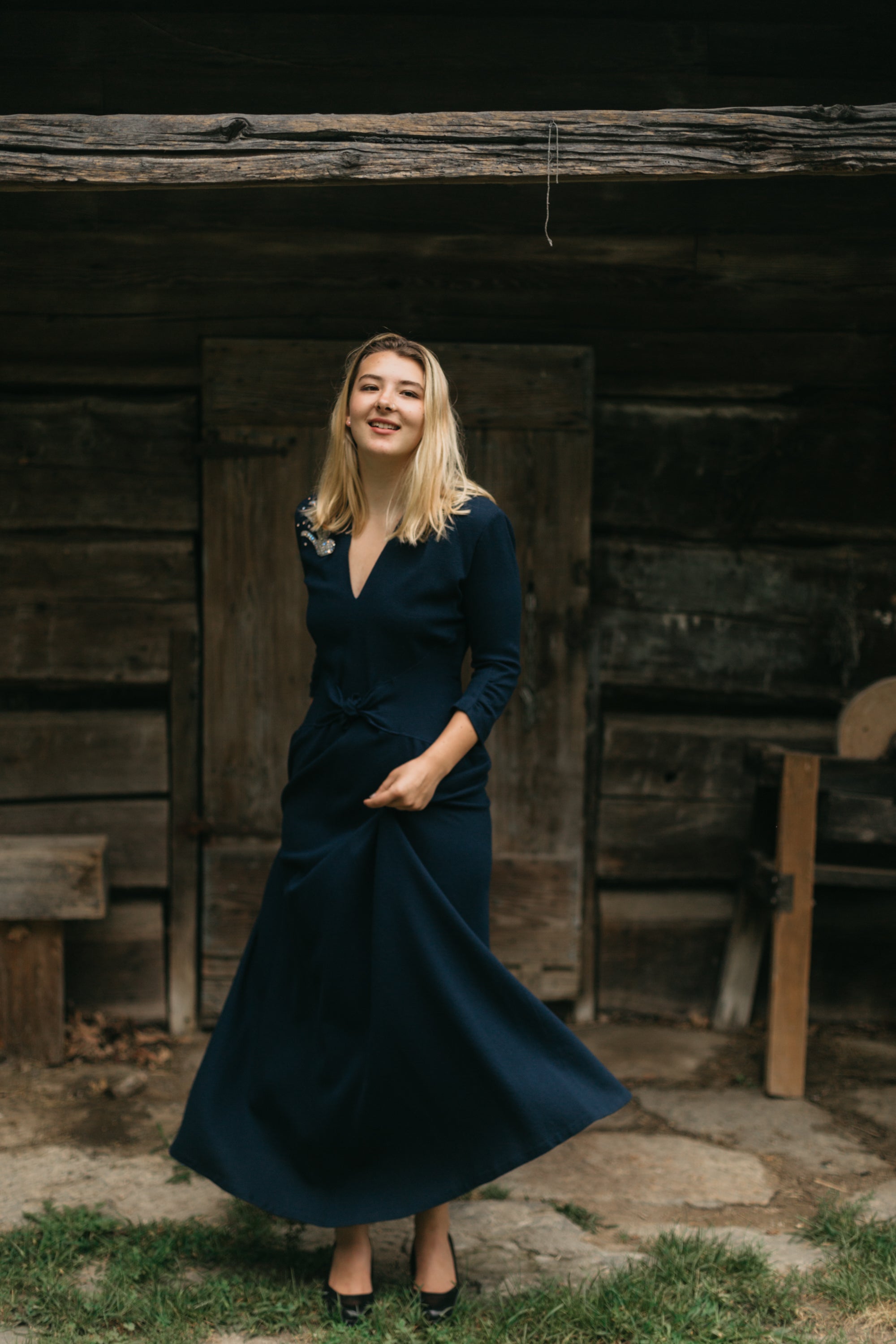 young blonde woman about standing in front of a small wooden building twirling the skirt if the 233 Glamour Girl Dress