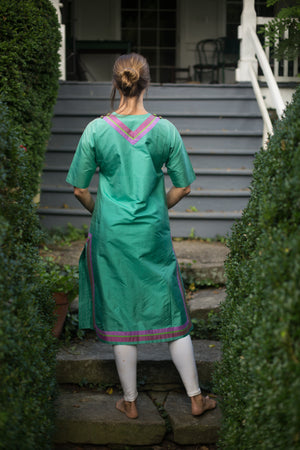 Model wears calf length kamiz and churidar.  She is standing at the bottom of stairs with back to camera.