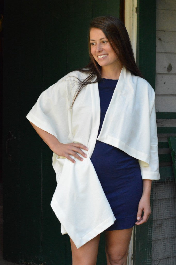 brunette  white woman with her right hand on her hip wearing a navy blue fitted dress underneath a white #271 Sunset Wrap that is draped over her shoulders.