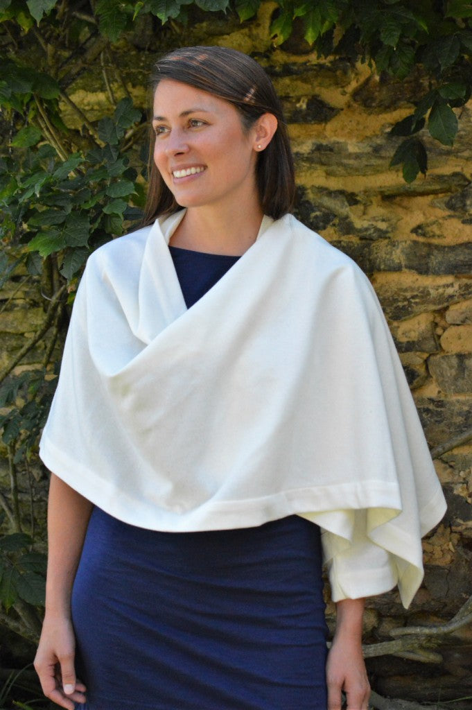 brunette  white woman with her right hand on her hip wearing a navy blue fitted dress underneath a white #271 Sunset Wrap that is draped over her shoulders.