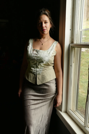 white woman standing next to window in sleevless corset top in light colored patterned fabric and skirt showing pattern use for women's corset top pattern make it yourself for cottagecore or romantic look