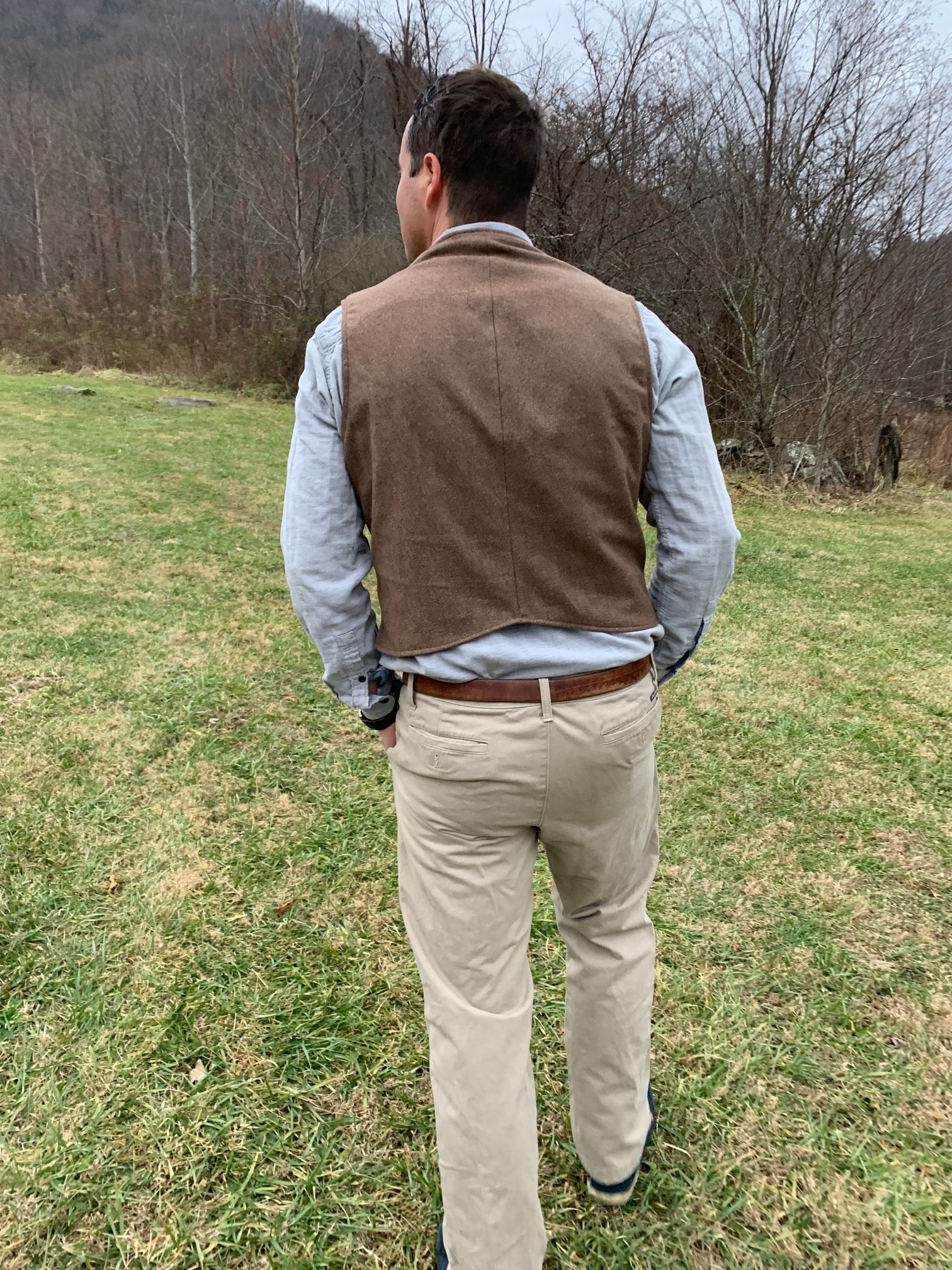Back view of man walking in a field wearing 222 Vintage Vests with no adjustable waist belt in the back.