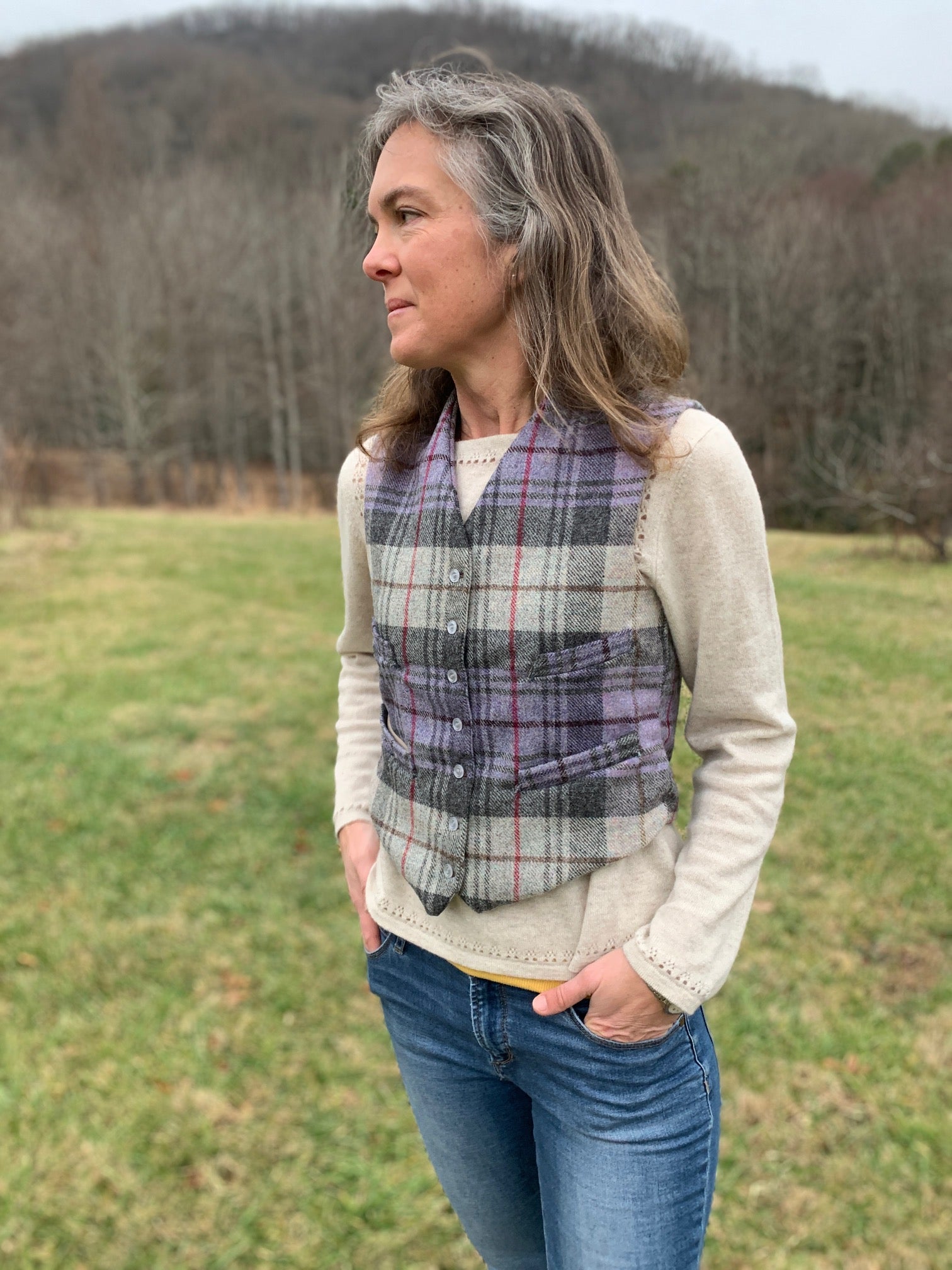 Woman standing in a field with hands in pockets looking to the left, wearing View A 222 Vintage Vests, collarless v-neck and four welt pockets.