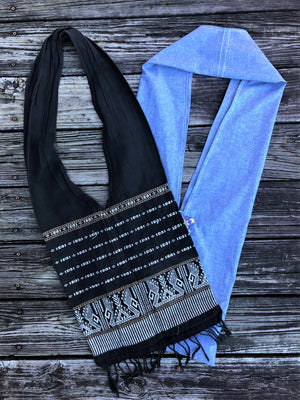 Two Thai shoulder sling bags - 1 black with woven white design on body of bag; 1 medium blue with small embroidery at top.