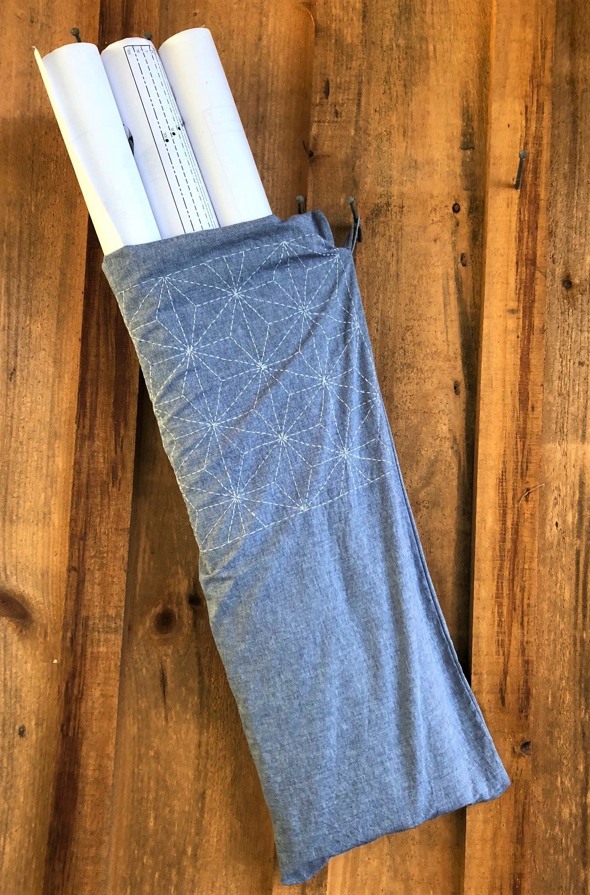 Blue Japanese Carpenters bag hanging on a wooden wall. Embroidered with white sashiko and holding rolls of paper.