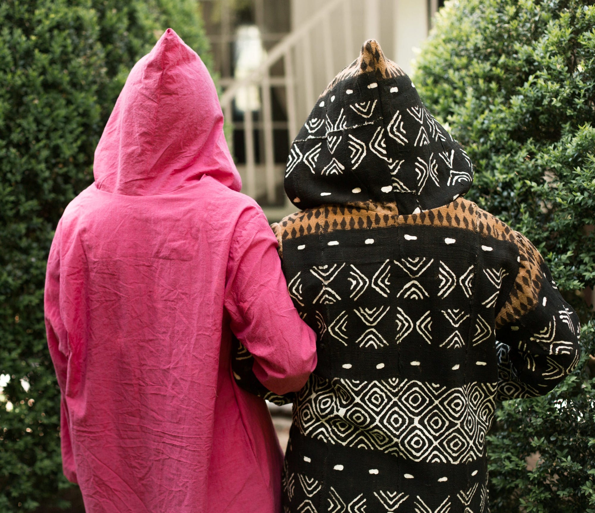 Back view of two women arms linked, surrounded by greenery wearing the Moroccan Djellaba with the hoods.