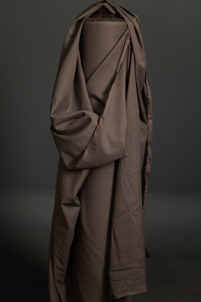 A swatch of organic cotton voile fabric in a grey brown color, draped elegantly against a dark background.