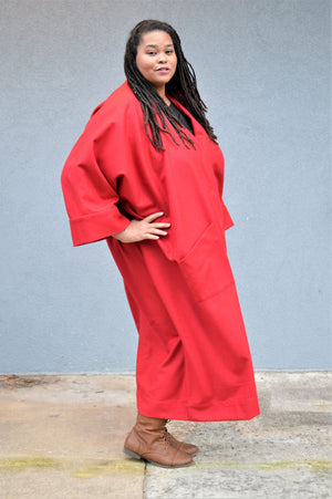 An African American woman, with hand on her right hip wearing the Basics Overcoat in a Scarlett Red wool. 